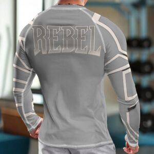 A long-sleeve compression shirt featuring a grey base with bold 'Rebel' typography and white geometric accents. The shirt is made with moisture-wicking fabric and a snug fit, designed for athletic performance and modern style.