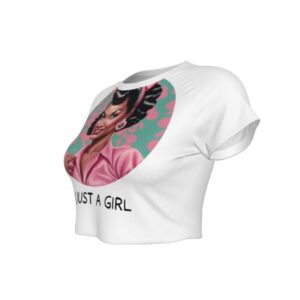 A white cropped t-shirt featuring a large circular graphic of a glamorous Black woman styled in 1950s pin-up fashion. She has glossy black curls, pink earrings, a headband, and a pink collared top. Below the image, the text reads “I’M JUST A GIRL” in bold black letters.