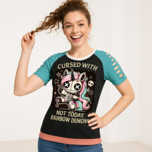 A women’s short-sleeve t-shirt with teal slashed sleeves and a light pink hem. The center graphic shows a stitched-up, gothic unicorn with multicolored hair, button eyes, and a stitched belly, holding up both middle fingers. Above it, the text reads “Cursed With” and below it says “Not Today, Rainbow Demons.” The background is black with small skull and star accents.