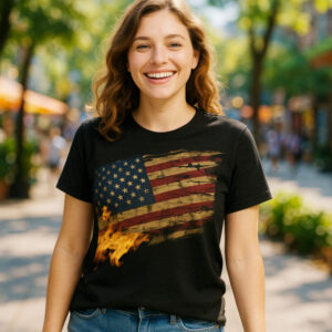 A black t-shirt with a distressed American flag printed across the front. Flames rise from the lower left corner of the flag, creating a visual of fire and endurance. The design represents strength, sacrifice, and national pride.