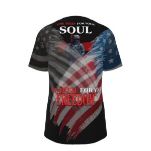 A black short-sleeve t-shirt with an all-over American flag graphic in muted red, white, and blue tones. On the back, a soldier silhouette overlays the flag with the large bold text: 'One Died For Your Soul, One Died For Your Freedom.' The design is strong and patriotic, blending faith and military honor.